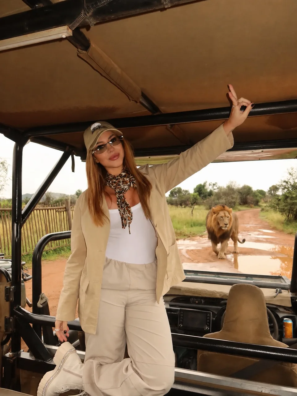 Mirella Sordi em um jipe de safári na África do Sul, com um leão ao fundo